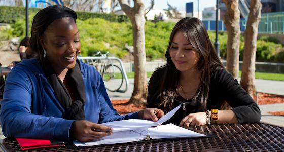 Two people talking outside over a binder of course information.