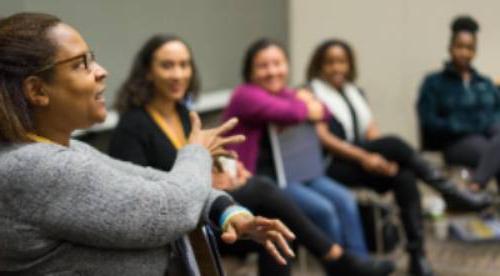 A woman describing something gestering with her arms while three other people in the room pay attention intently.