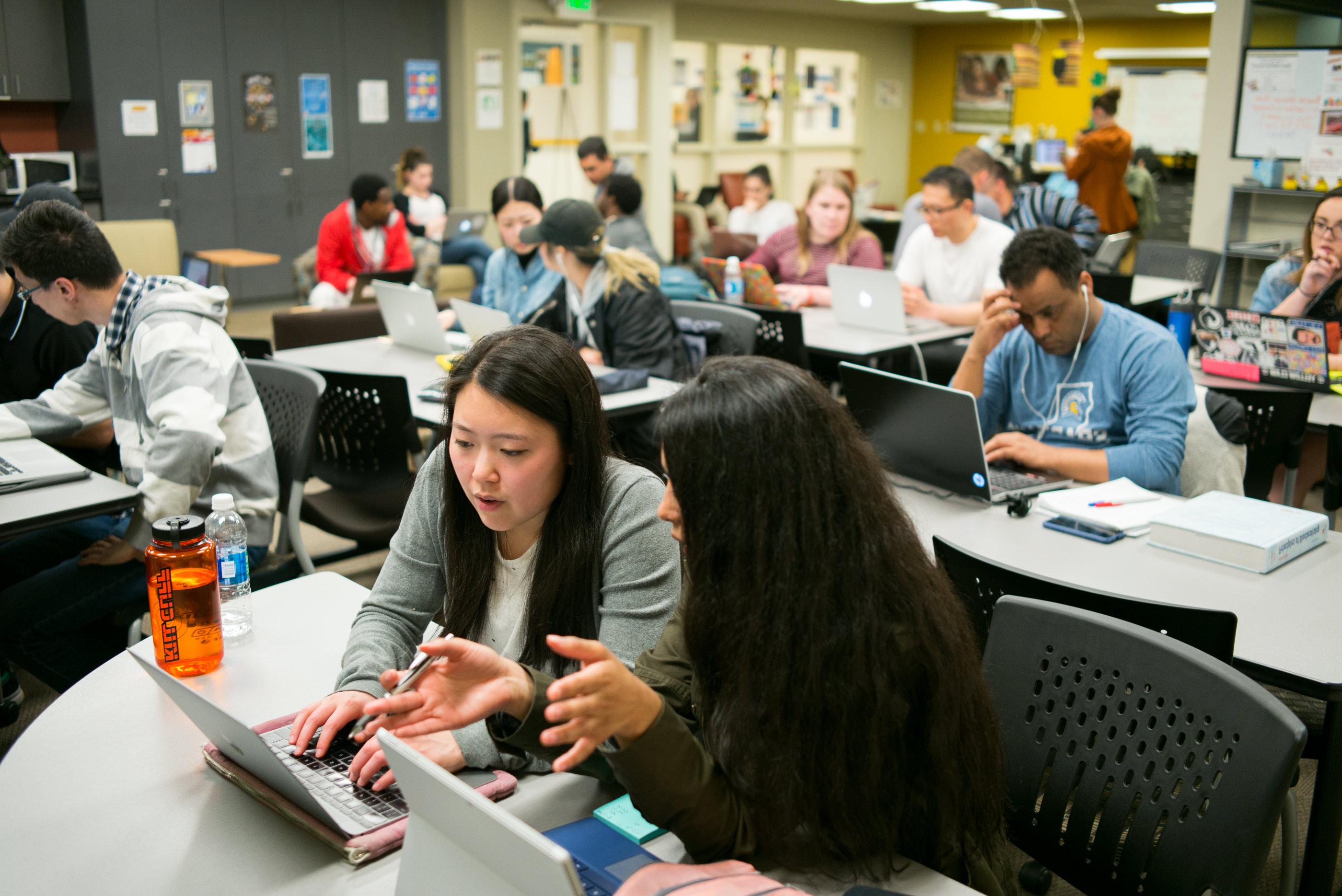 Students sit in a classroom looking at laptop computer while working together.